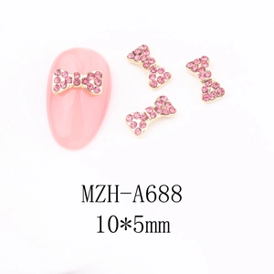 Detail of 10x5mm gold bow nail charm with pink rhinestones for festive manicure art