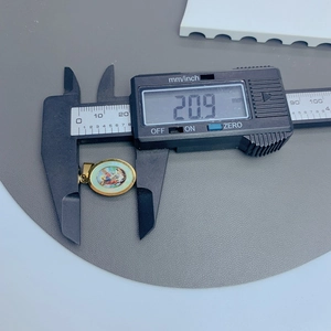 Digital caliper measuring the 20.9 mm height of a golden Guadalupe pendant