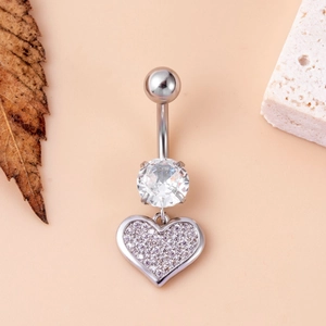 Silver belly button ring with large zircon and heart pendant on stone and leaf background