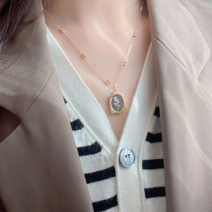 Elegant rose pendant necklace on gold chain with model wearing neutral autumn layers