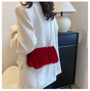 Detail view of burgundy velvet crossbody bag with golden chain strap on white blazer