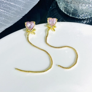 Detailed macro shot of long tassel earring with pink heart gem and golden bow decor