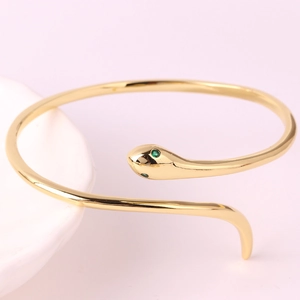 Minimalist gold snake open bangle with green gemstone eyes and polished metal finish