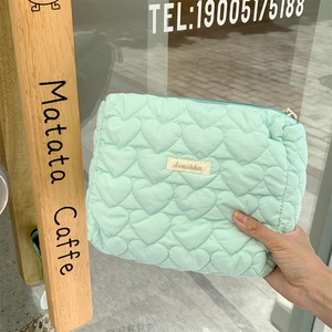 Detail of mint green quilted makeup bag with heart pattern and woven label branding