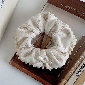 Close-up of beige plush scrunchie featuring cartoon bear patterns and cute white bow detail
