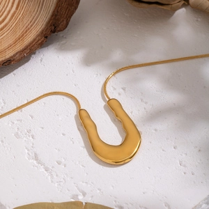 Collier doré à pendentif en U irrégulier avec chaîne serpent sur un fond de texture blanc