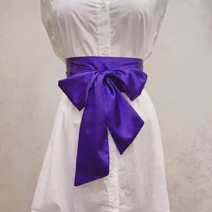 Détail d'une ceinture en satin violet nouée en nœud sur une robe chemise blanche, brillant