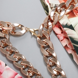 Macro shot of rose gold Cuban link chain with lobster clasp on floral satin fabric