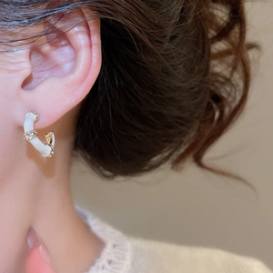 Detailed close-up of C-shaped gold bamboo earrings with white enamel and sparkling crystals