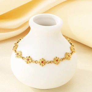Dettaglio ravvicinato del bracciale dorato a fiori con pietre rosse su un vaso bianco