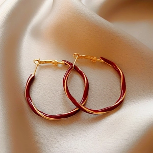 Detail of twisted gold and burgundy enamel hoop earrings on champagne silk fabric