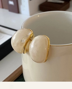 Close-up of vintage C-shaped cream resin earrings with elegant gold-plated edges