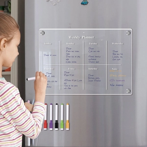 Child writing on a magnetic acrylic weekly planner with 6 colorful markers on a fridge