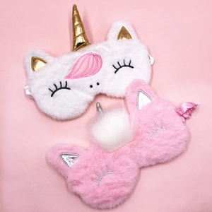 Detail of plush unicorn sleep masks with golden and silver horns on a pink background