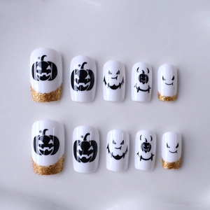 Faux ongles Halloween avec base blanche, motifs citrouilles noires et paillettes dorées