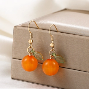 Creative orange fruit earrings with green leaves and gold hooks on satin background
