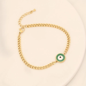 Détail du bracelet en chaîne dorée avec pendentif œil maléfique vert sur un plateau crème