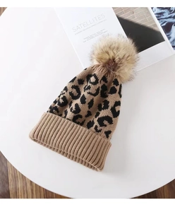 Macro detail of leopard print knit beanie featuring a fluffy pompom and ribbed cuff