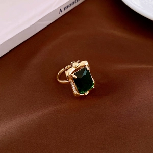 Macro shot of gold ring with emerald cut green stone and diamond accents on brown silk