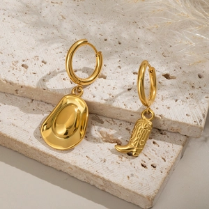 Detail of asymmetric gold earrings with cowboy hat and boot pendants on a textured stone