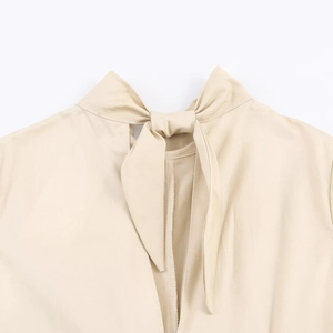 Detail of elegant V-neckline with a bow tie design on a beige midi dress fabric