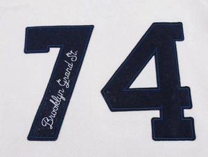 Detail of dark blue number 74 flocking patch with white Brooklyn embroidery on white cotton