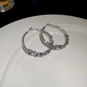 Detail of silver hoop earrings with frosted texture and zircon pearls on white plate
