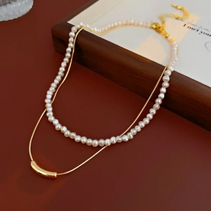 Detail of layered gold snake chain and pearl necklace on a dark vintage surface