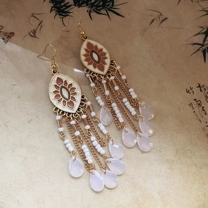 Detail of bohemian long tassel earrings with white enamel flowers and beaded chains