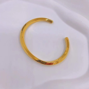 Detail shot of the polished golden Mobius twisted open cuff bangle on white fabric