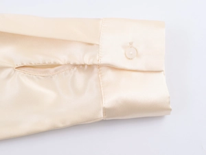 Detailansicht der beigefarbenen Satin-Manschette mit einem Knopf und feinen Nähten am Ärmel