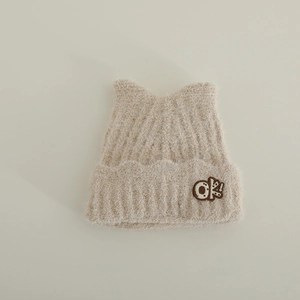 Close-up of soft beige plush knit hat with cat ears and embroidered patch detail