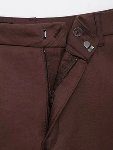 Detail of dark brown trousers showing the zipper, button, and metal hook closure system