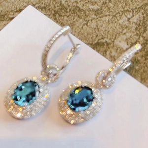 Elegant blue oval sapphire earrings with pavé diamond halo in silver metallic setting
