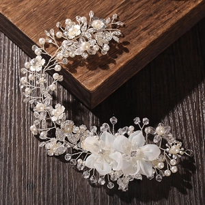 Detailed close-up of bridal hair comb with pearls and white flowers on dark wood surface