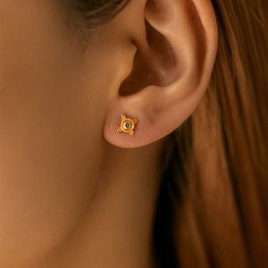 Macro shot of 18K gold geometric starburst earrings with blue stone detail on ear