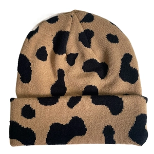 Detailed view of brown cow print knit beanie hat with black spots on white background