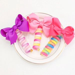 Three colorful bow telephone wire hair ties with spiral bands in a white ceramic dish