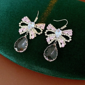 Macro shot of luxury bowknot earrings with pink rhinestones and dark grey drop pendants