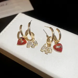 Gold plated dog and red heart stud earrings with zircon stones on white leather