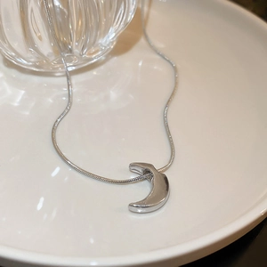 Detailed view of silver crescent moon pendant with sleek snake chain on a white plate