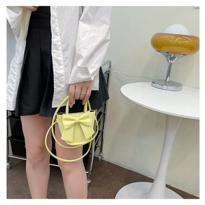 Close-up of yellow mini crossbody bag with bow decoration held by model in interior