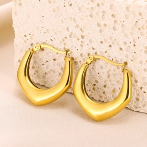 Detailed macro shot of gold hollow geometric earrings on a natural beige stone background
