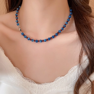 Detail of blue stone beads and red spacers on a minimalist necklace worn with lace collar
