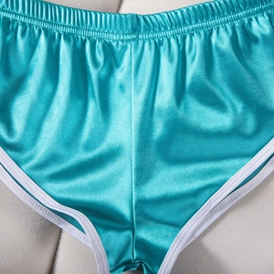 Dettaglio ravvicinato degli shorts sportivi in raso color ottanio con piping bianco
