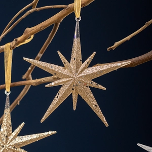 Nordic gold star Christmas ornament with glitter finish hanging on a rustic branch