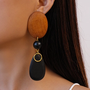 Detail of wooden geometric oval and teardrop earrings worn by a model in close-up shot