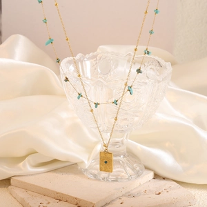 Double-layered turquoise gold necklace with engraved evil eye pendant on a silk background