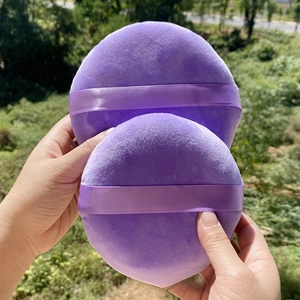 Detail of two large purple velvet powder puffs with ribbon handles for body makeup