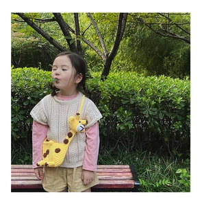 Detail of cute yellow hand-knitted giraffe crossbody bag for toddler girls in a park